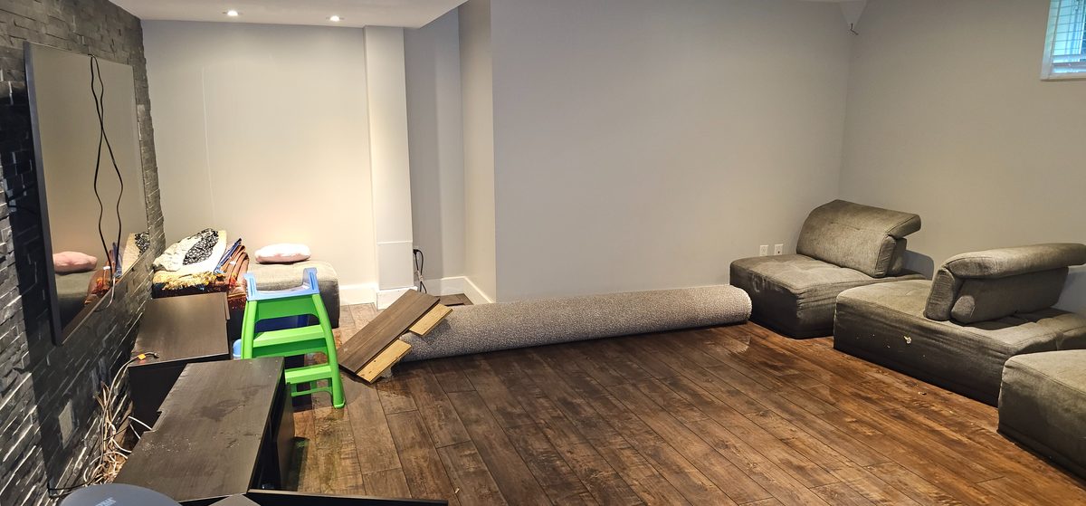 Flooded basement family room with water-damaged flooring and furniture