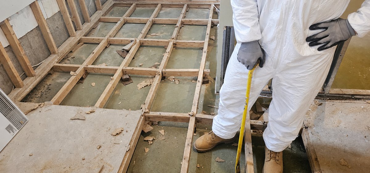 Technician in protective suit working on exposed subfloor after flood damage